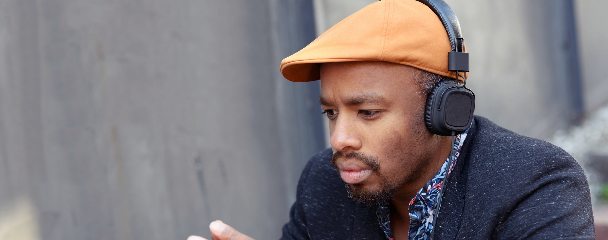 Black man in orange driving cap with black over the ear headphones looking down deep in thought